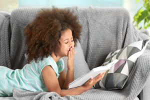 Cute African girl reading book on couch