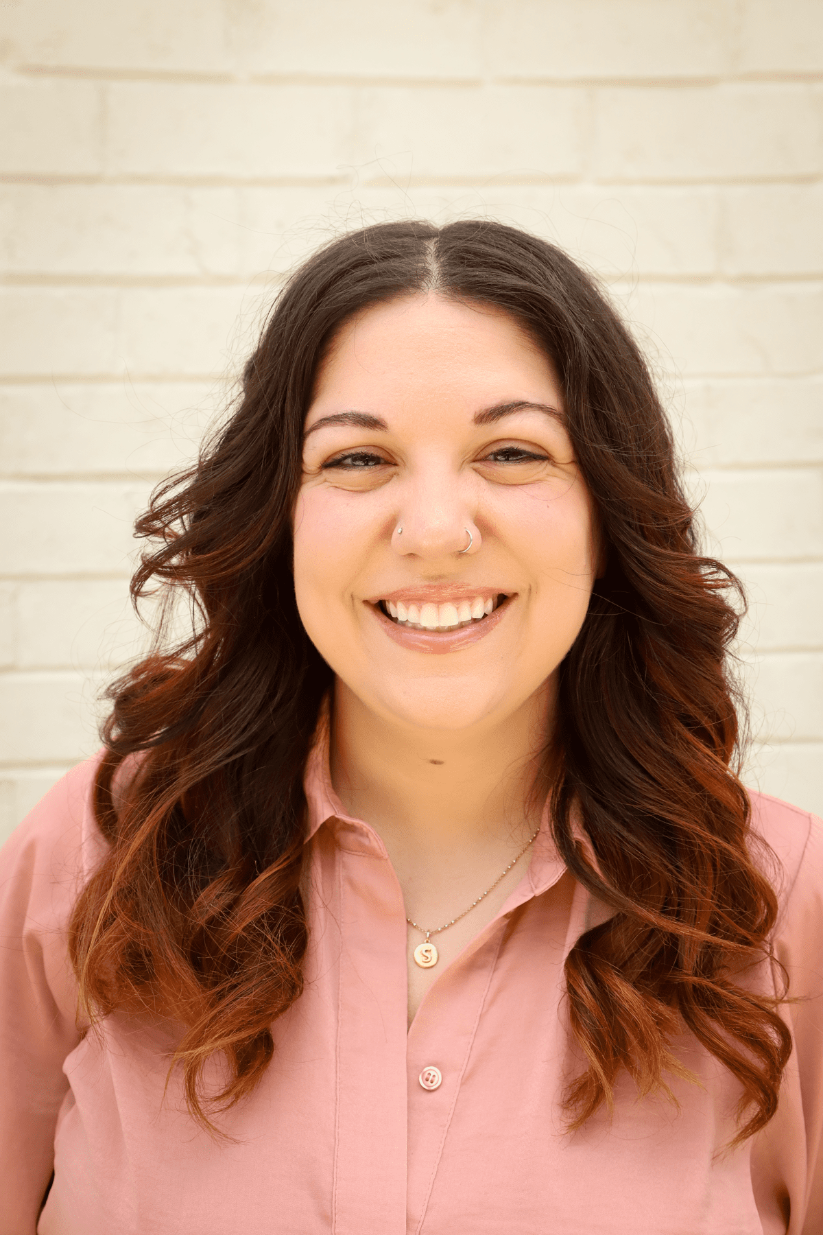 Juliana Peres, a latina woman with brown hair that's red at the tips and a pink blouse. She is looking at the camera smiling.