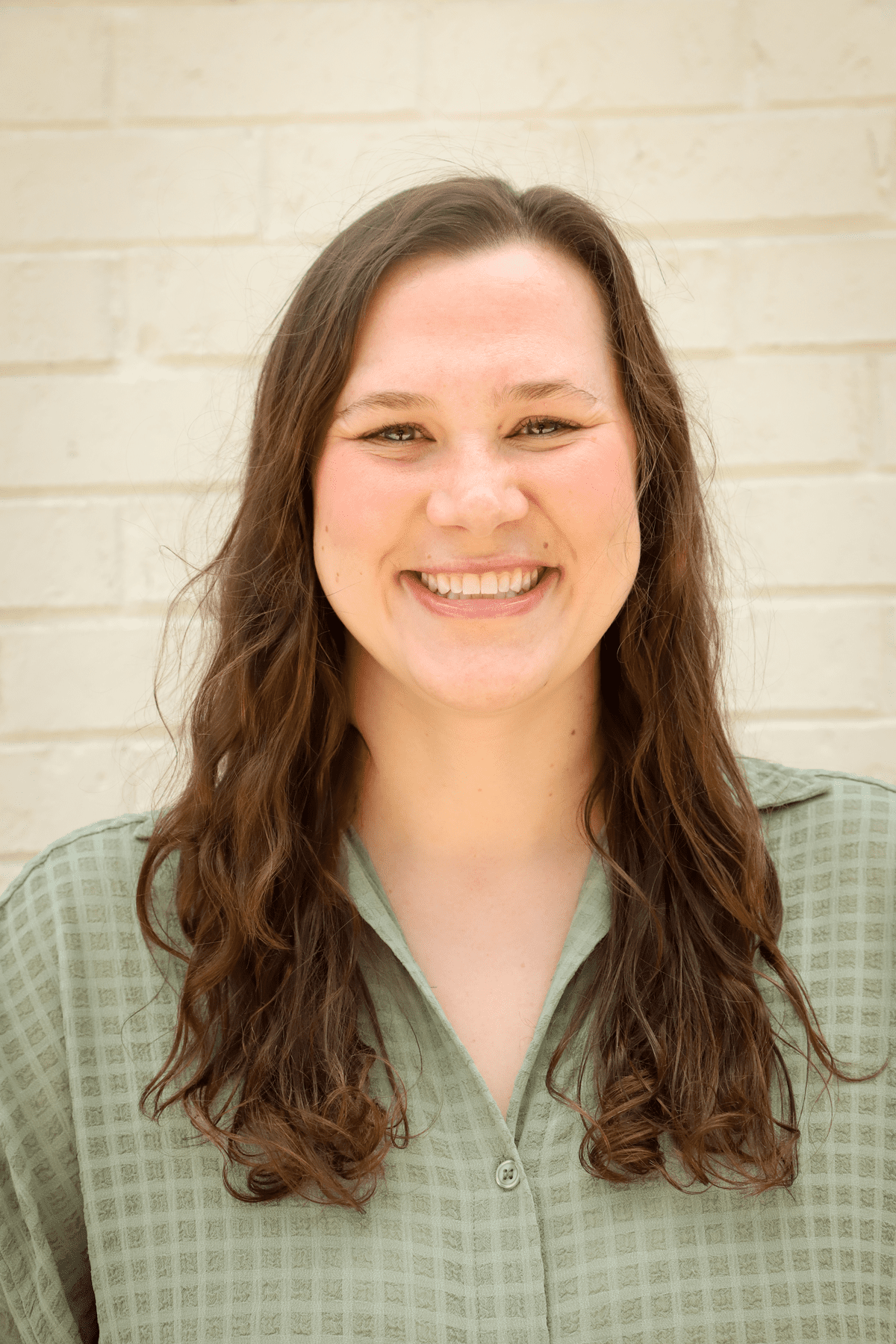 Katy Brath Botelho, a white woman with brown hair wearing a green button up shirt. She is looking at the camera smiling. 