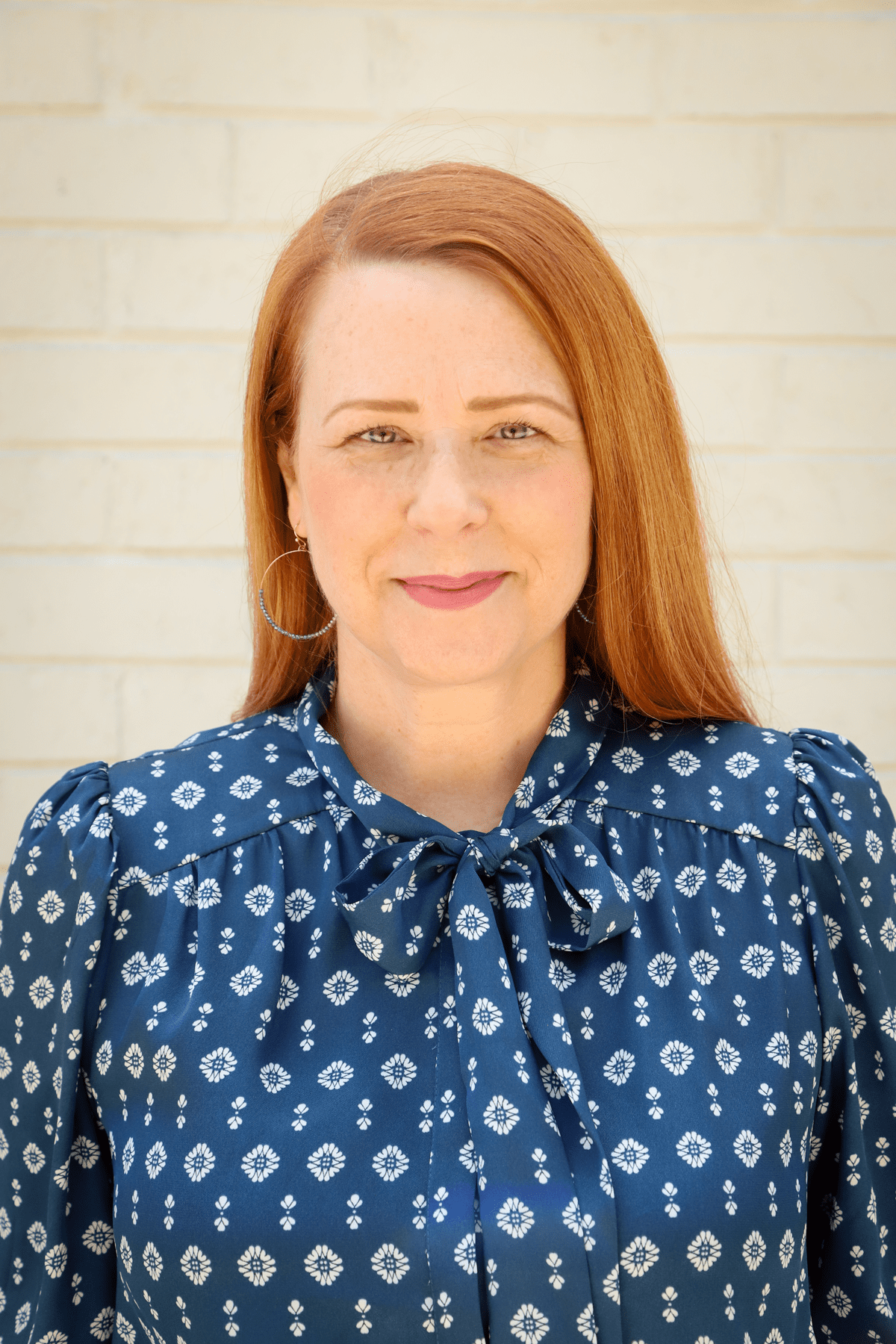 Kelly Cates, A red-headed white woman wearing a blue patterned blouse. She is looking at the camera with a slight smile.
