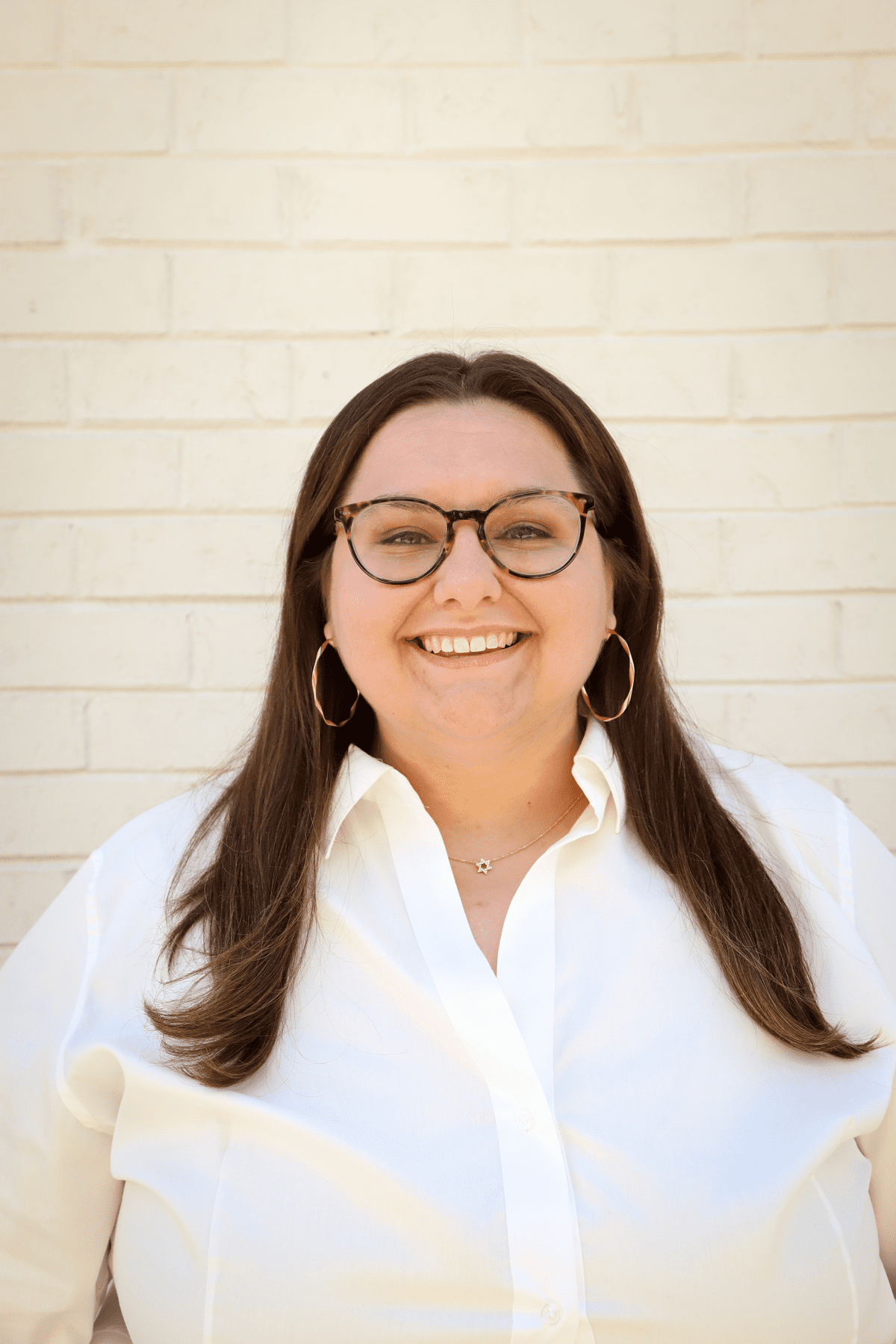 Samantha Weissman, a white woman with dark brown hair and glasses wearing a white blouse. She is looking at the camera smiling.