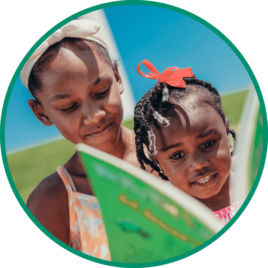 A little girl picking holding a book in her hands and picking out another one from a book shelf. She is looking at the book she's picking up and starting to smile.