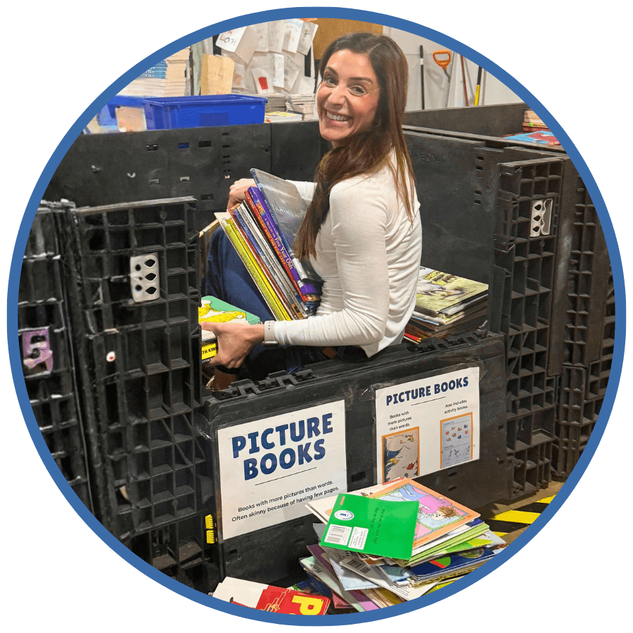 Photo of a white woman in a black bin labeled "Pictured books" holding a stack of books smiling at the camera. The photo is in a dark blue circular frame.
