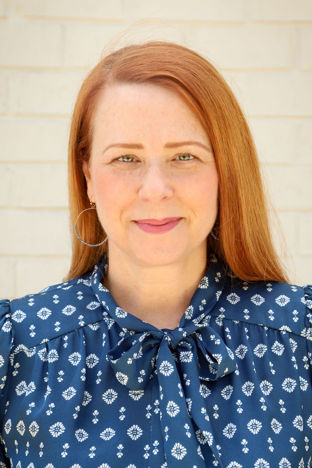 Kelly Cates, A red-headed white woman wearing a blue patterned blouse. She is looking at the camera with a slight smile.